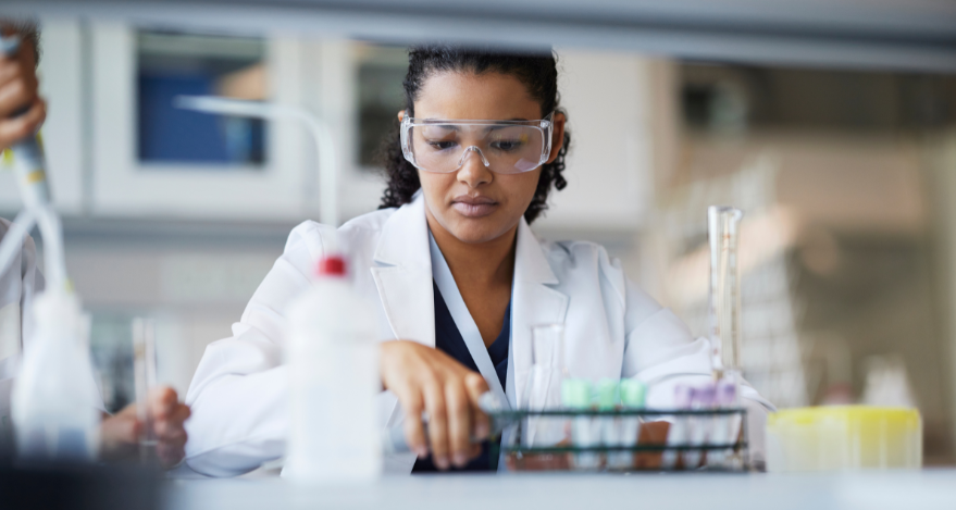 A female researcher with goggles examines test tubes in a scientific setting