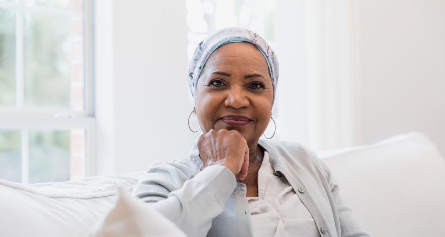 A woman with cancer, wearing a head covering, smiles at the camera.