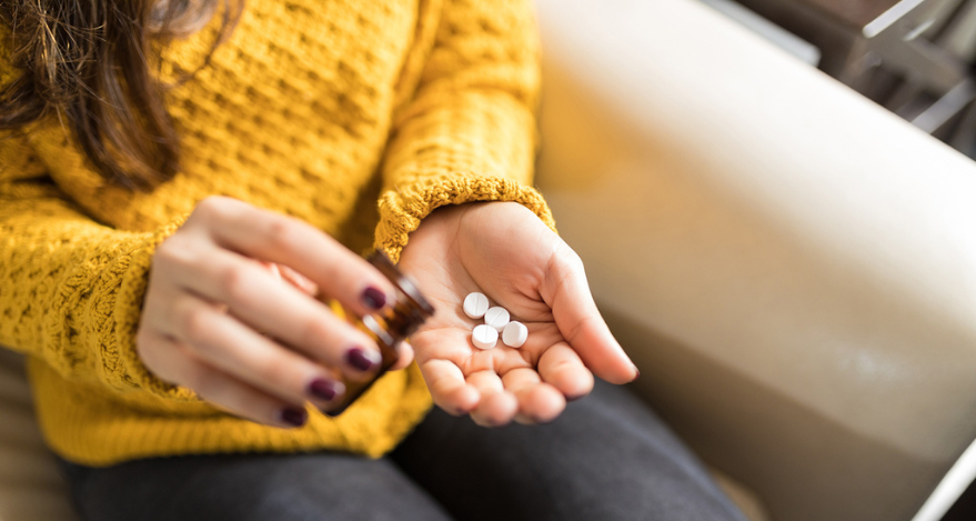 A person holds a prescription medication bottle and pours out four pills into their other hand.