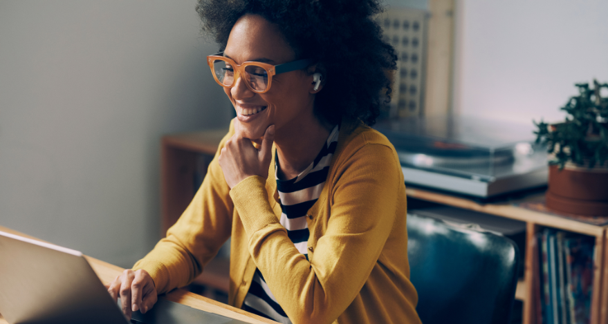 A woman with glasses smiles while looking at a laptop computer
