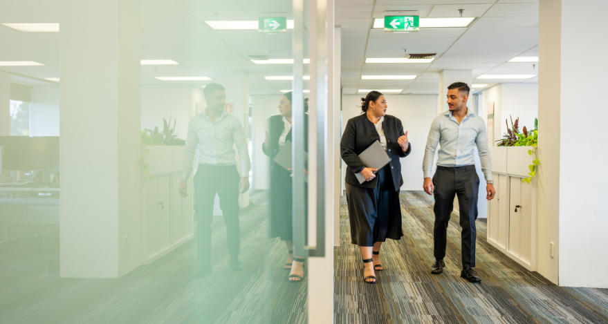 Two people walk side by side while talking in an office environment
