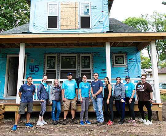 10 Individuals Standing in Front of a Partially-Built Home in Blue T-Shirts